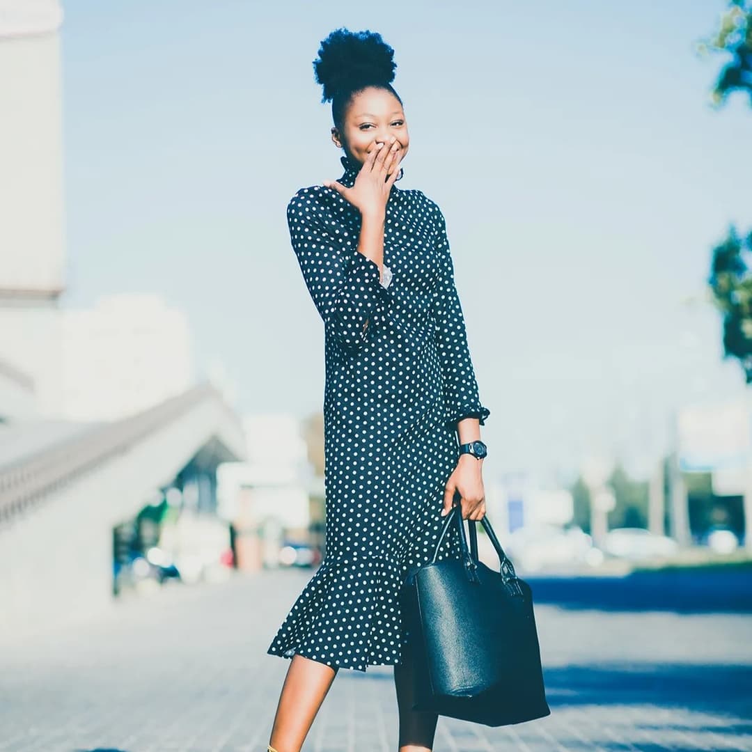 Woman standing holding black purse.