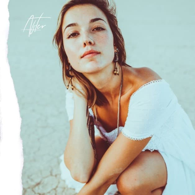 Woman sitting in sand hand on neck.