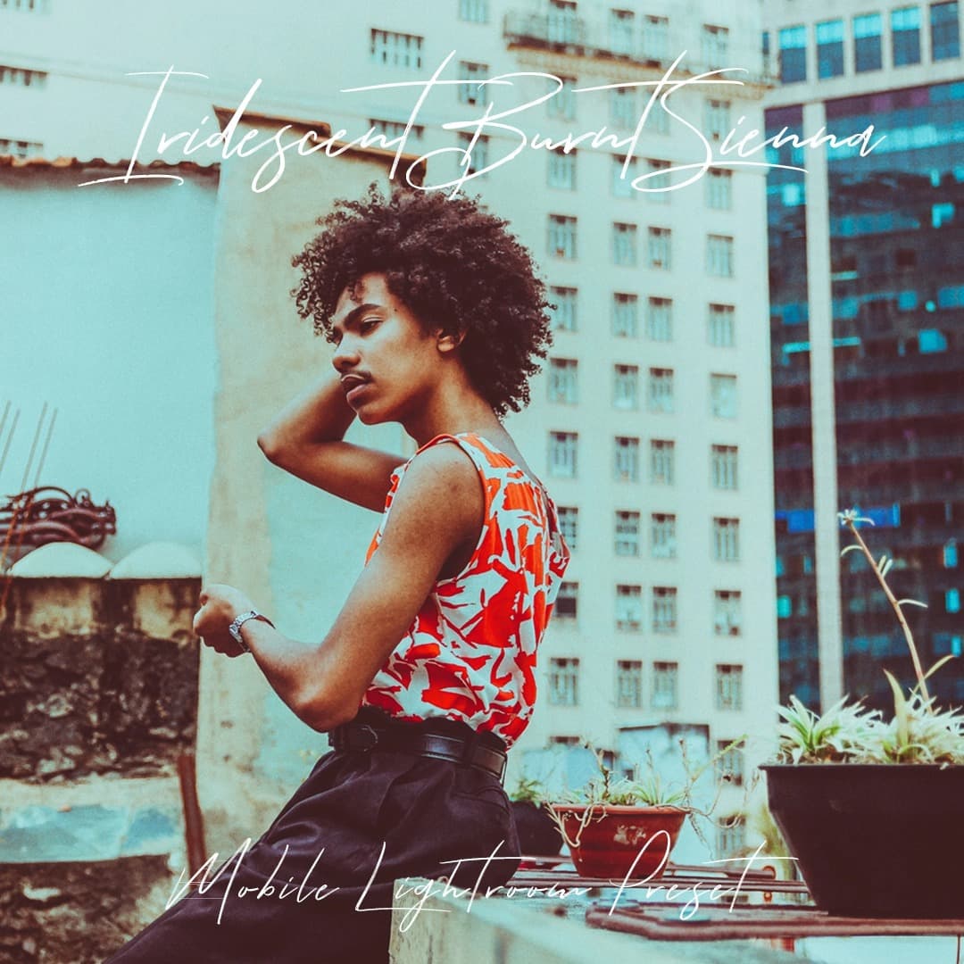 Black guy sitting on rooftop touching his hair.