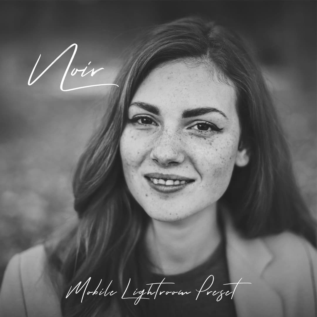 Freckled woman smiling at the camera in black and white.