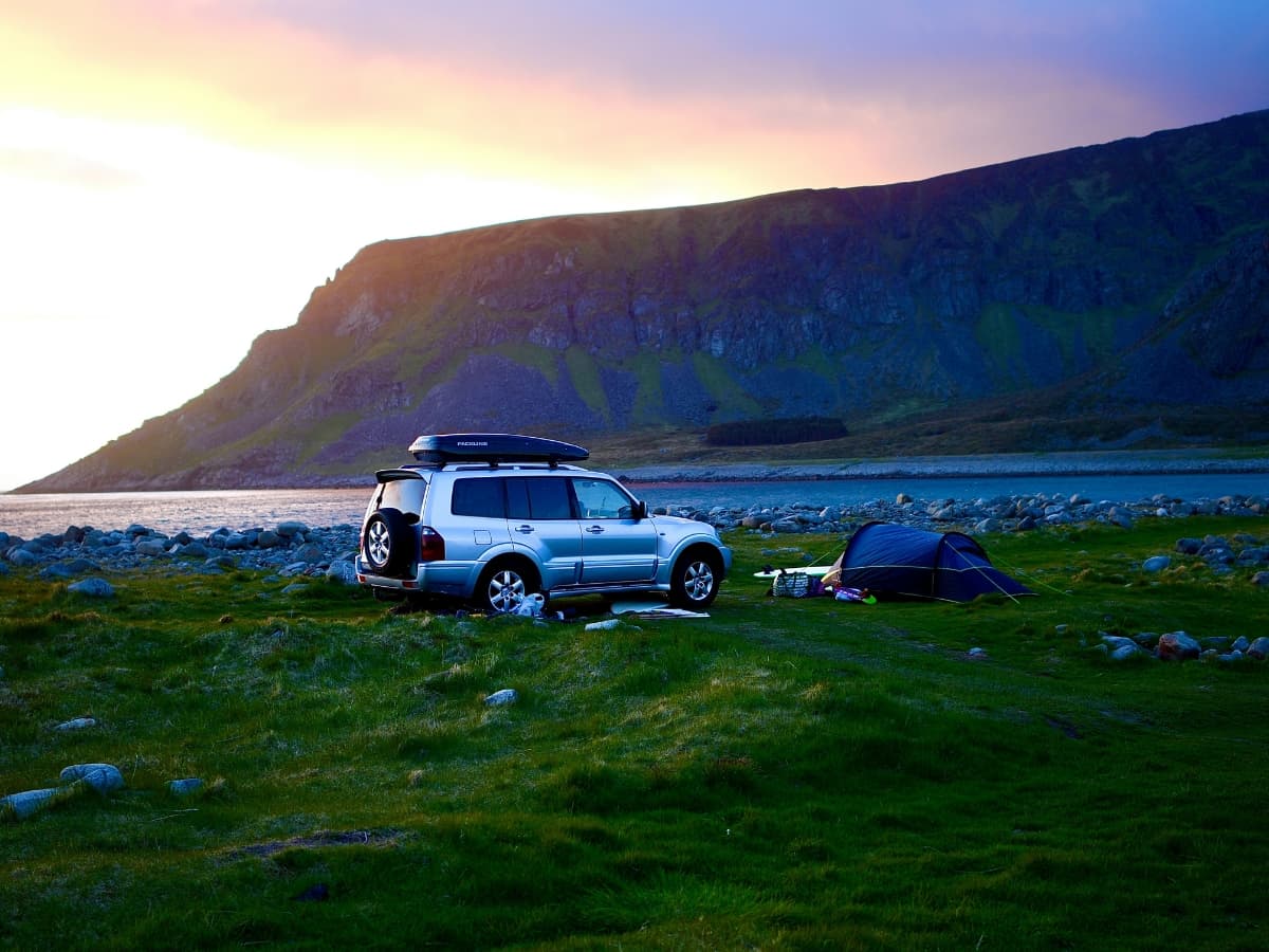 Automotive photo of a car near a hillside and tent.