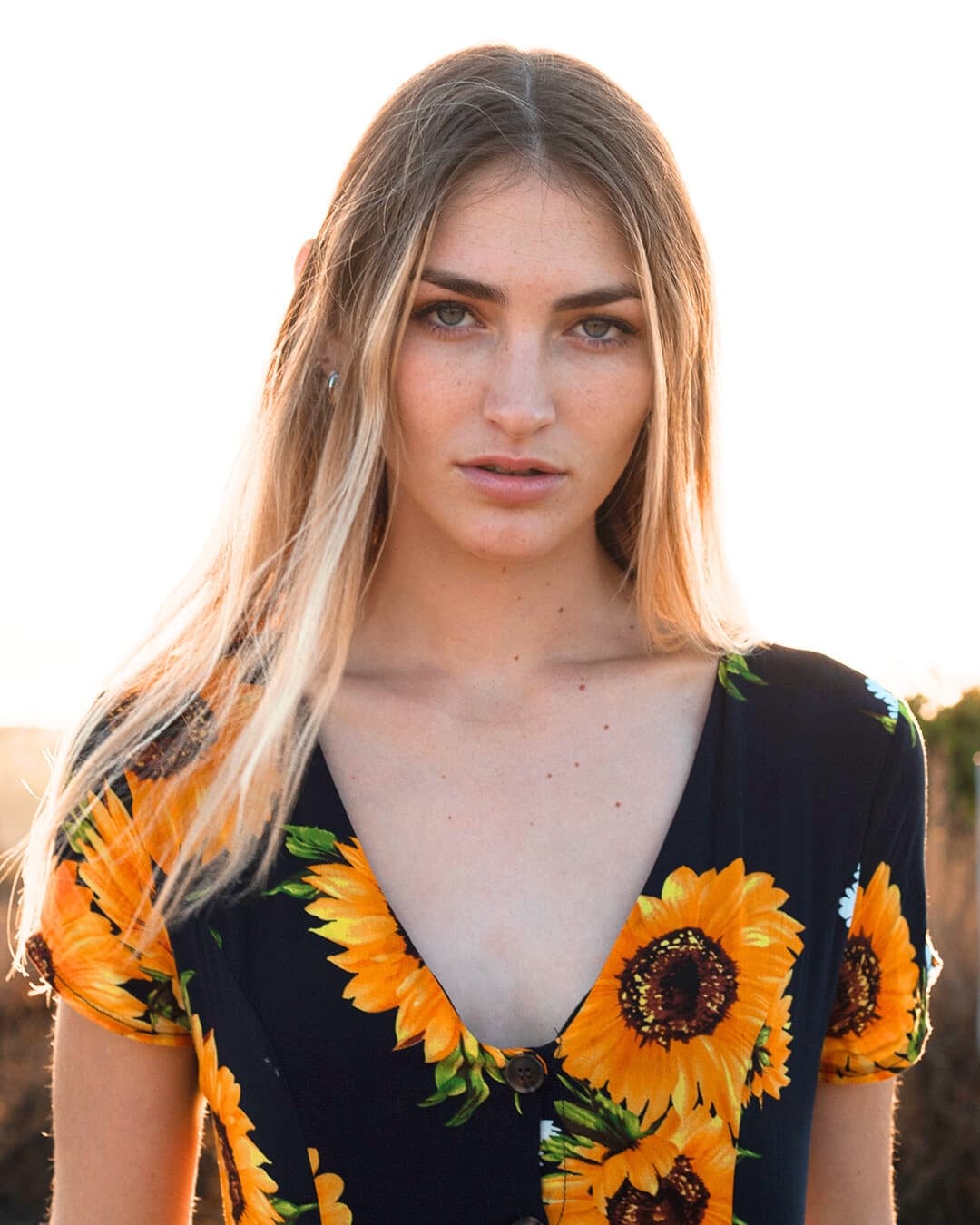 Girl in flower dress in front of sun.