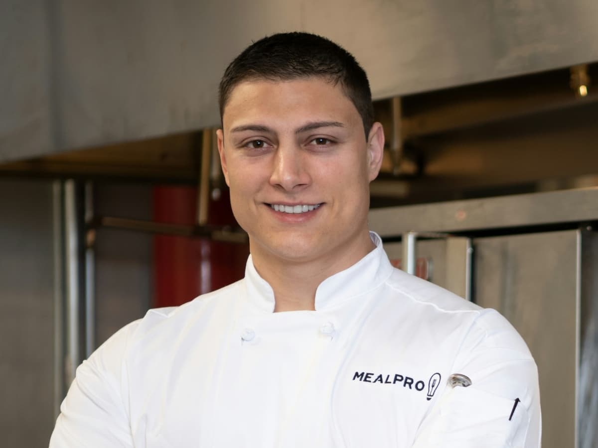 Chef standing in kitchen smiling at camera.