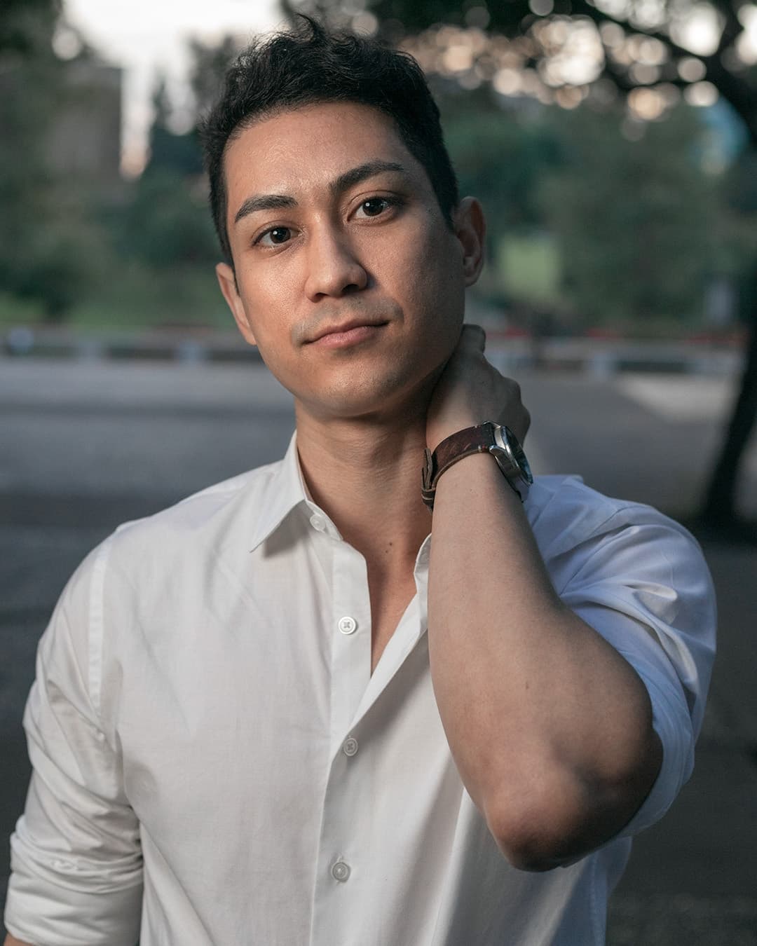 Man posing in white dress shirt with hand on neck.