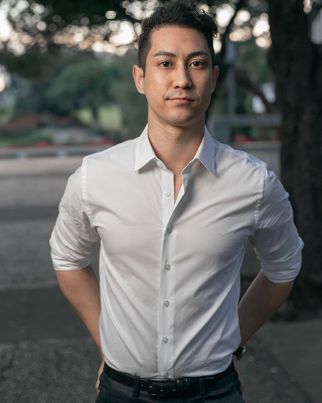 Man posing in white dress shirt with his hands behind his hips.