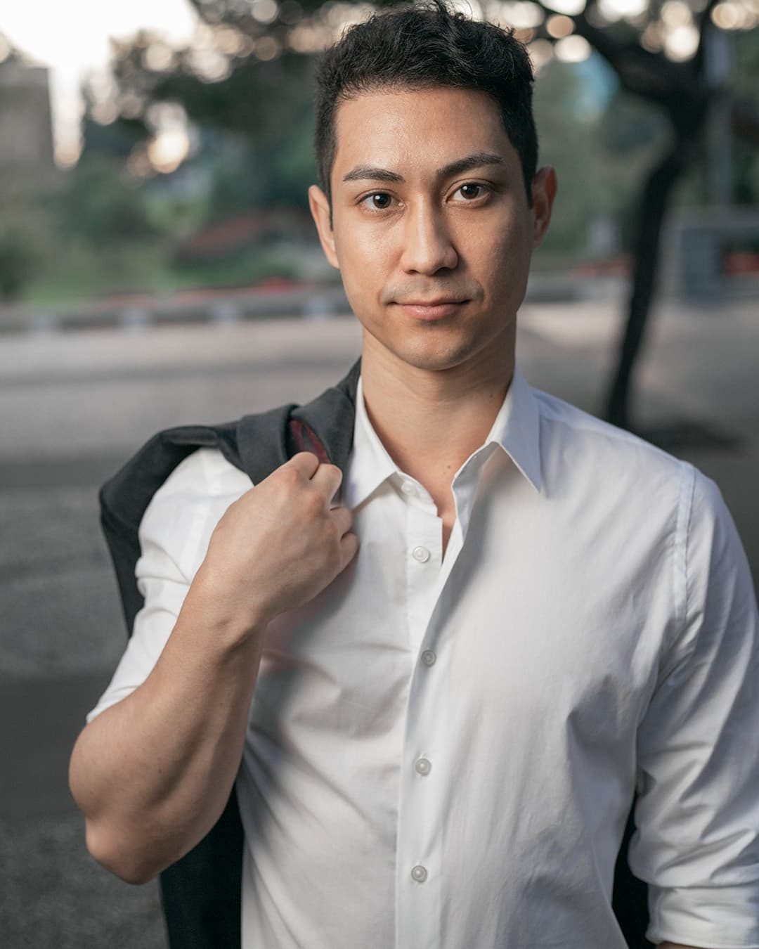 Man posing in white dress shirt with a jacket over the shoulder.