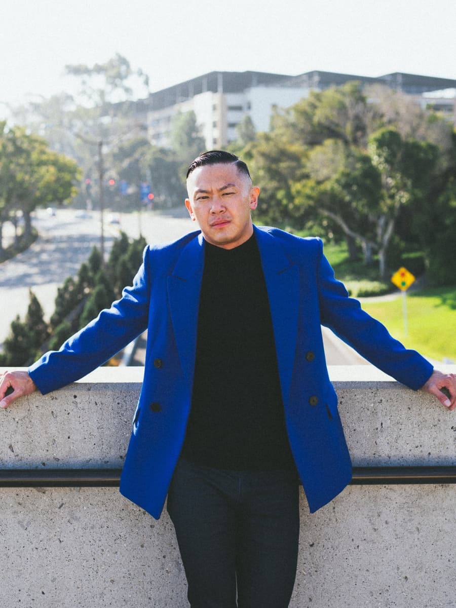 Man posing in blue suit with both hands spread.