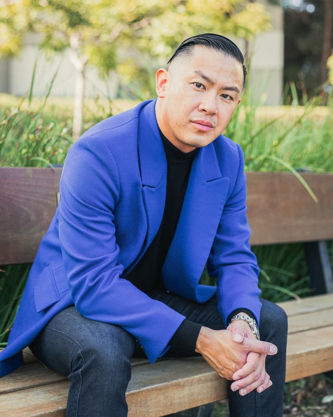 Man posing in blue suit sitting down leaning into his arms.
