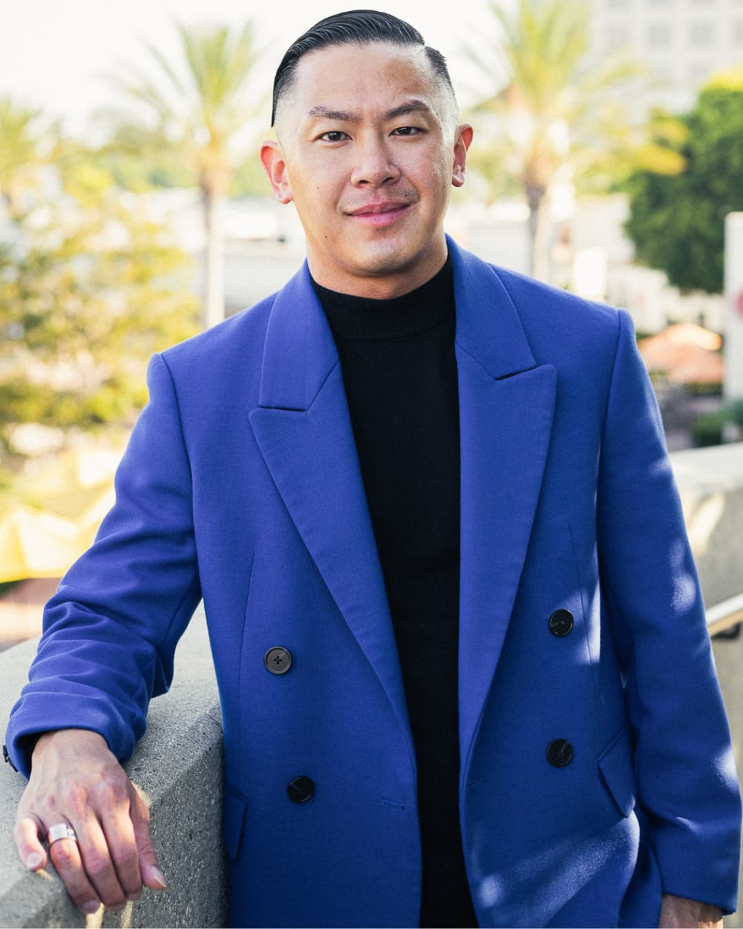 Man posing in blue suit leaning his arm on an arm rest.