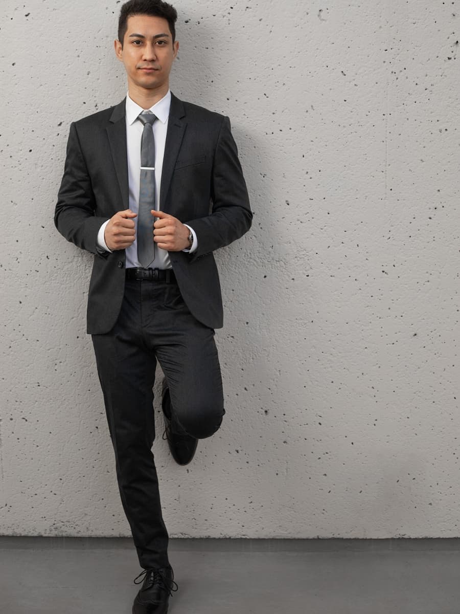 Man posing in suit face forward leaning on wall.