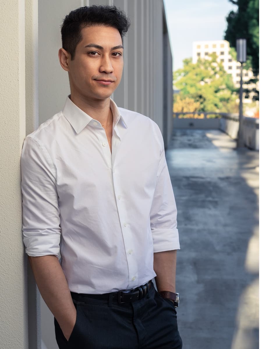 Man posing in white dress shirt leaning sideways on wall.