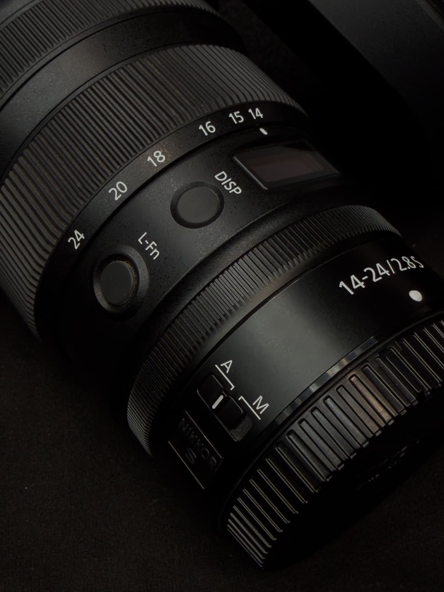 High-detail texture shot of the Nikon Z 14-24mm f/2.8 S showing the ribbed rubber pattern of the zoom and manual focus rings contrasted against the metallic knurling of the custom control ring and the L-Fn button