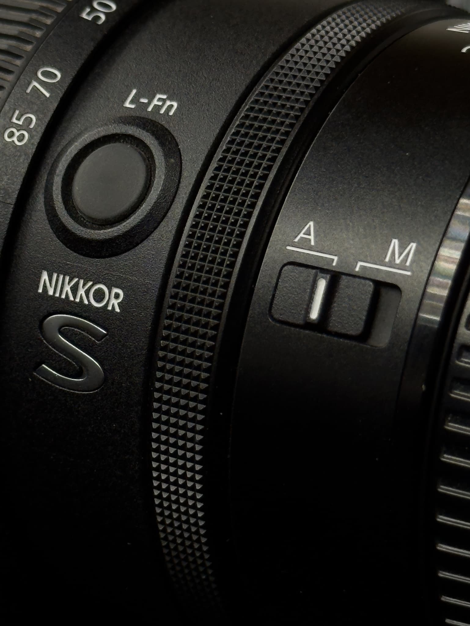 High-detail texture shot showing the distinct cross-hatched knurled texture of the third independent customizable control ring on the Nikon Z 24-120mm f/4 S, contrasted against the matte finish of the primary aluminum-alloy/composite barrel