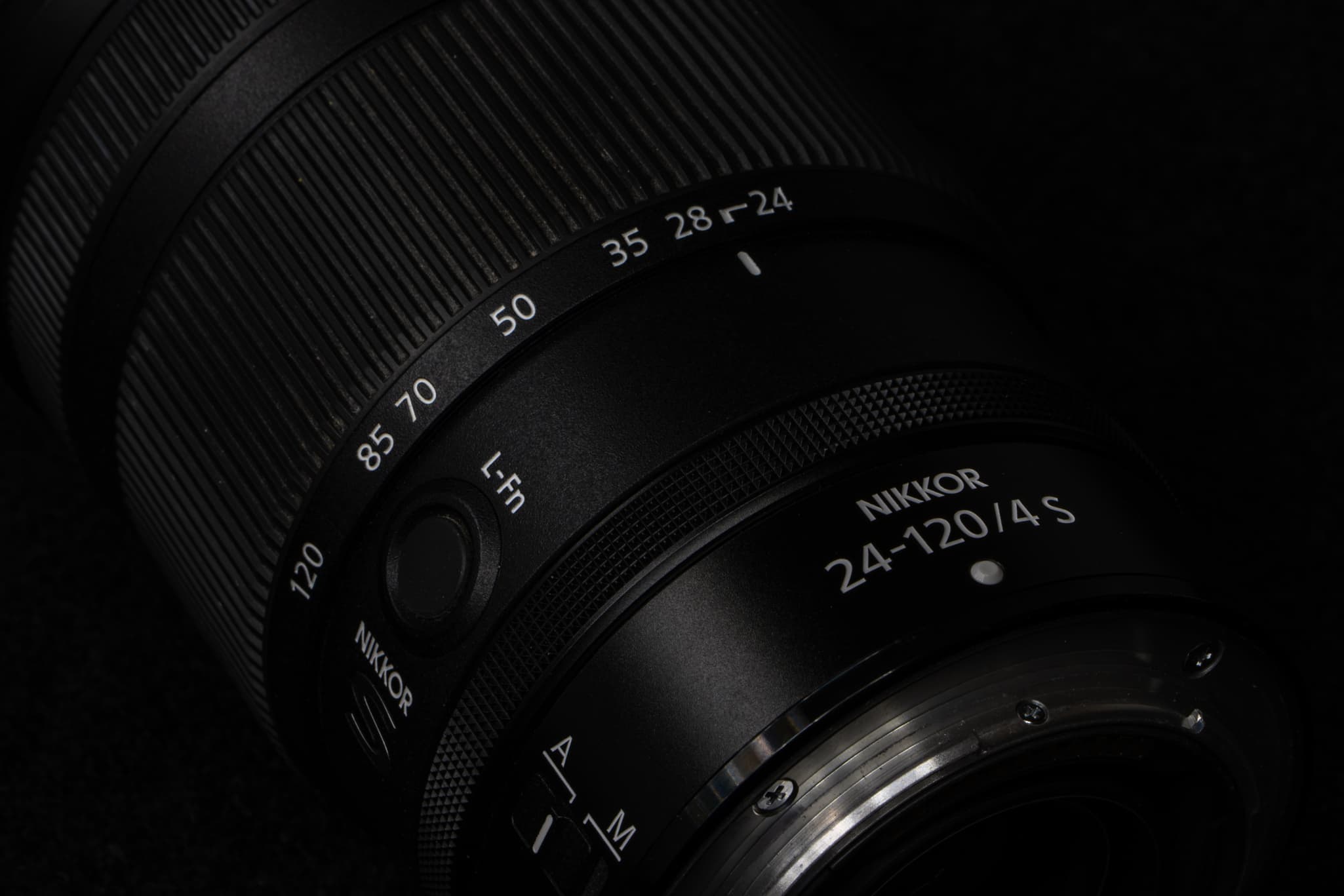 High-detail texture shot showing the distinct cross-hatched knurled texture of the third independent customizable control ring on the Nikon Z 24-120mm f/4 S, contrasted against the matte finish of the primary aluminum-alloy/composite barrel
