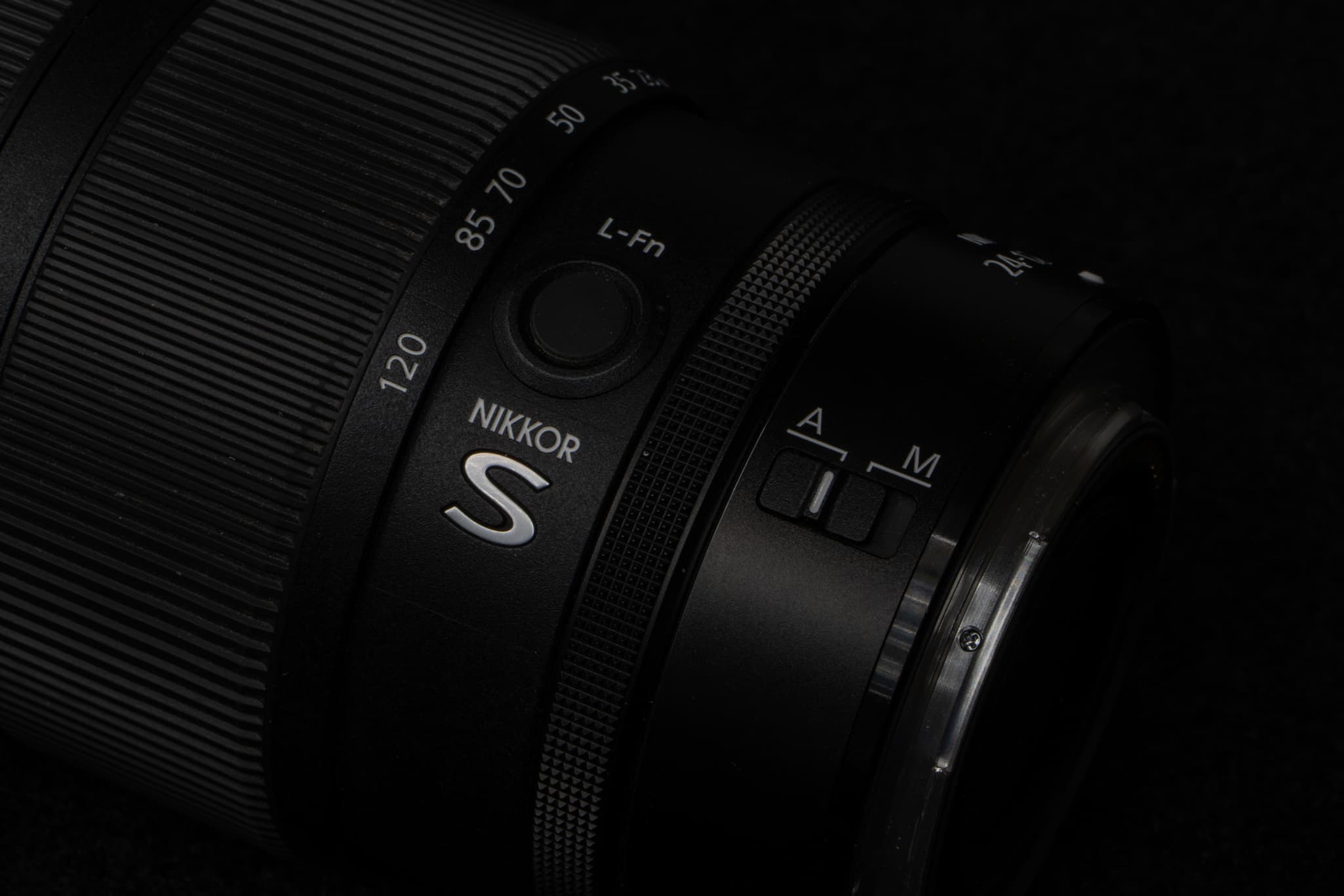 High-detail texture shot showing the distinct cross-hatched knurled texture of the third independent customizable control ring on the Nikon Z 24-120mm f/4 S, contrasted against the matte finish of the primary aluminum-alloy/composite barrel