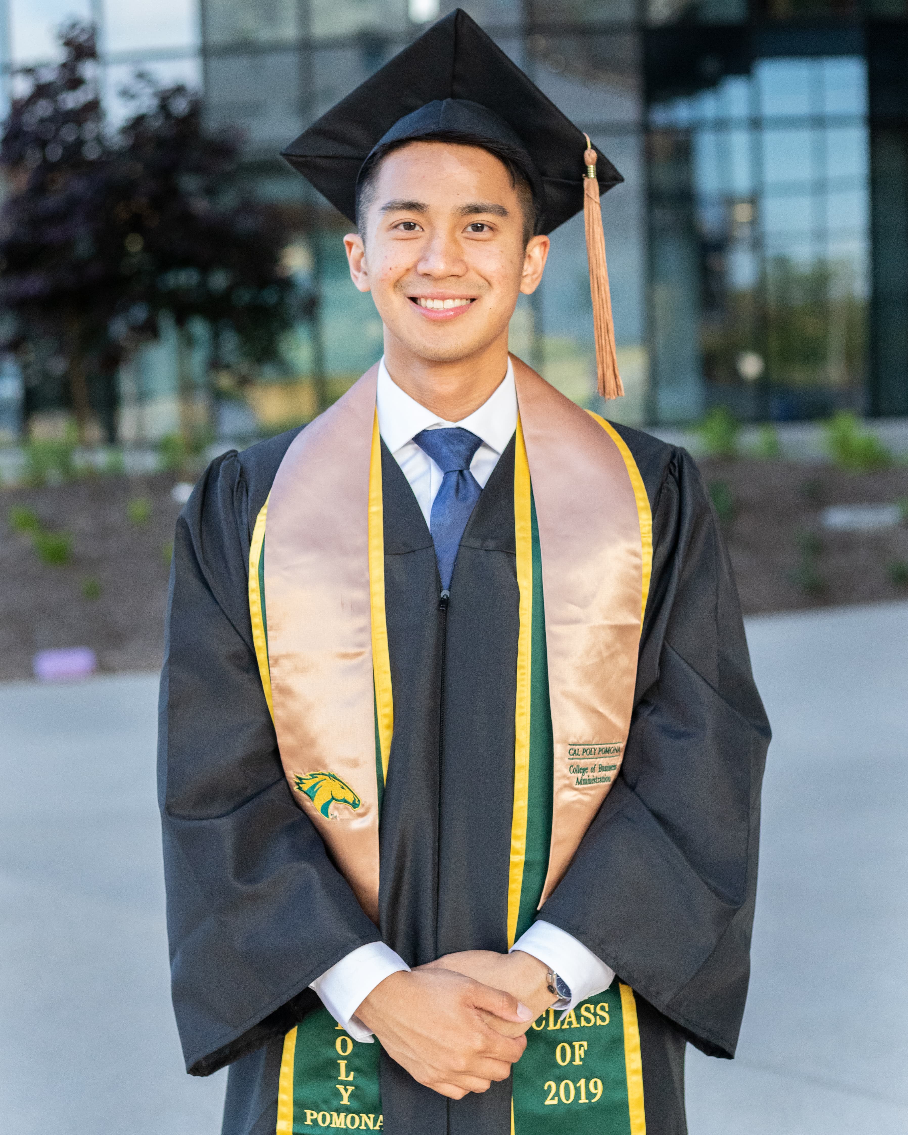 Man standing in Cal Poly Pomona graduation outfit smiling in the sun.