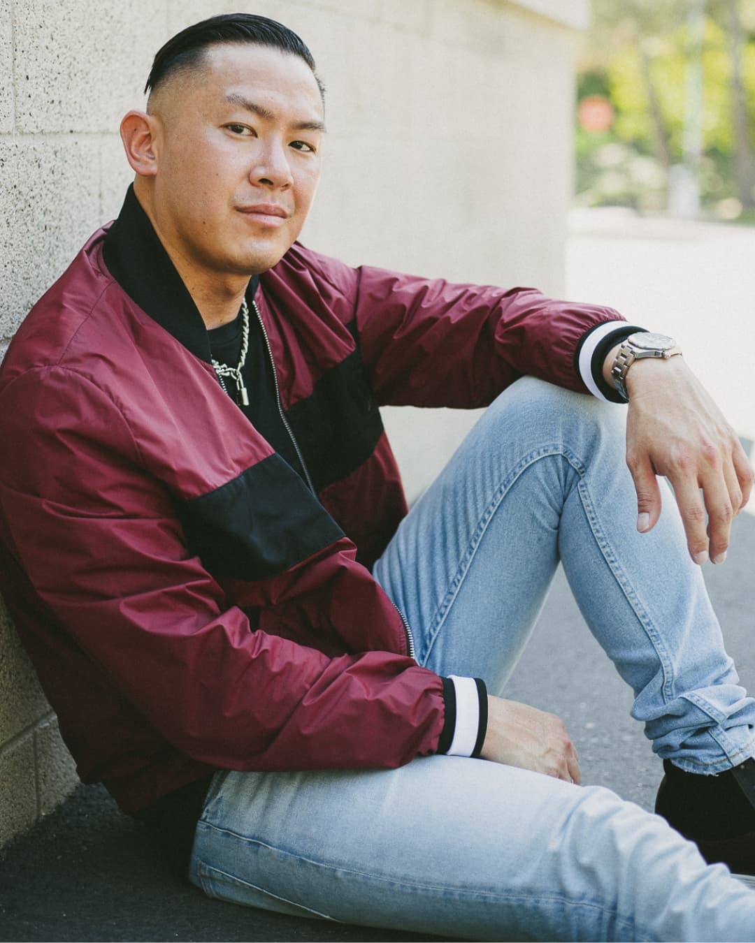 Man posing in red jacket sitting down with one knee up.
