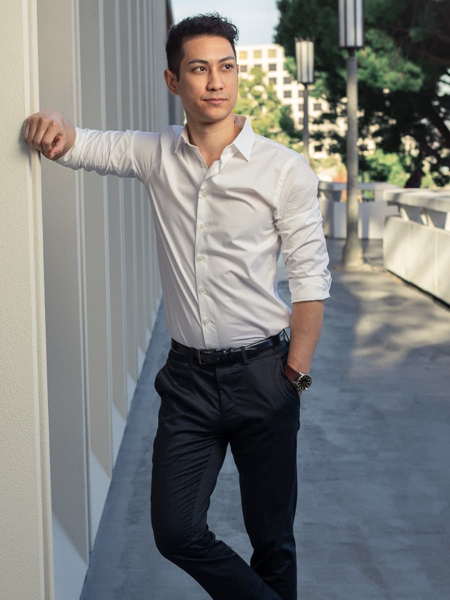 Man posing in white dress shrit reclining on wall.