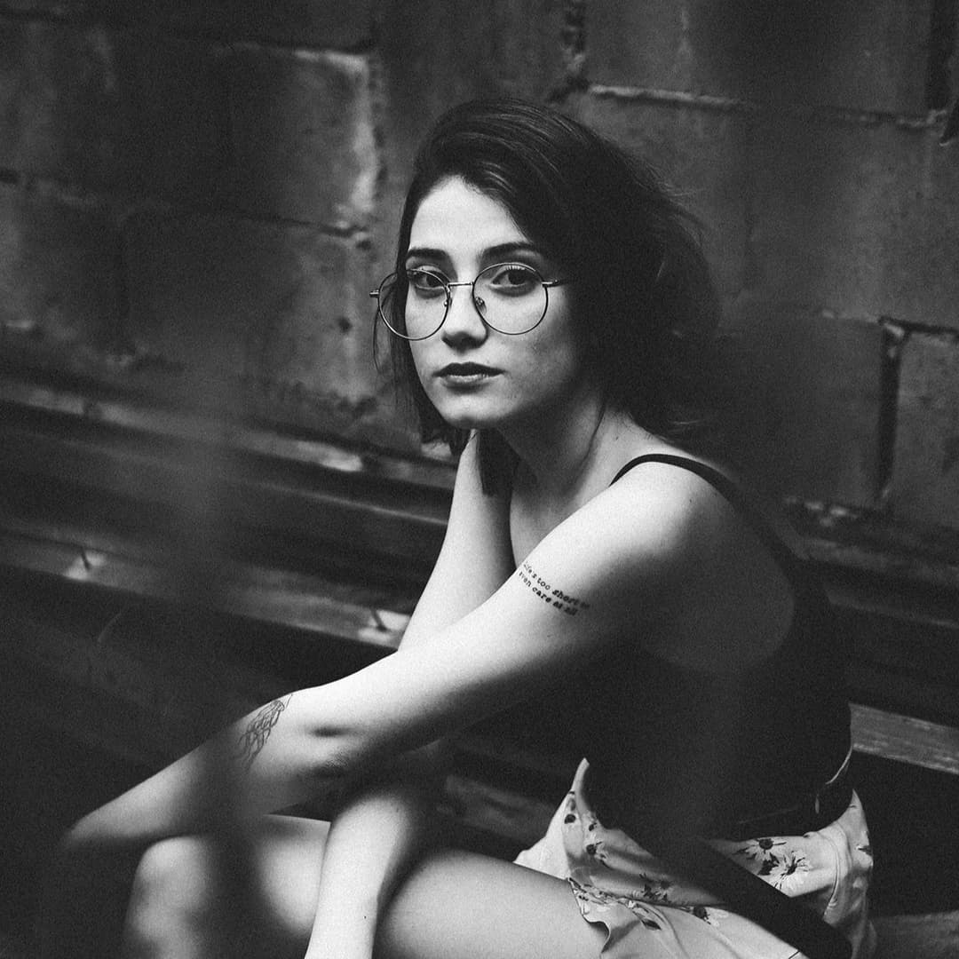 Woman with glasses sitting down looking up at camera.