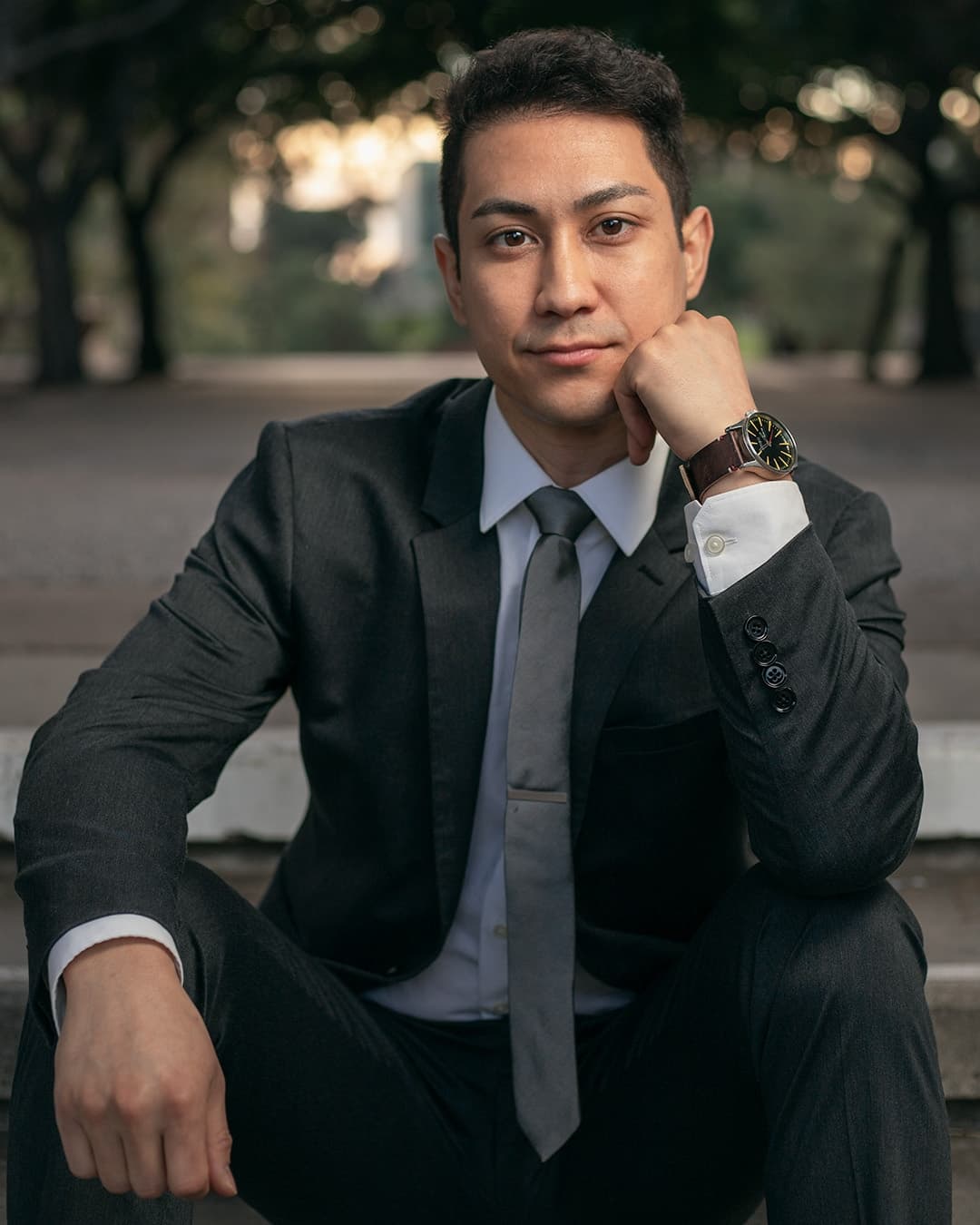 Man posing in suit sitting one hand on chin.