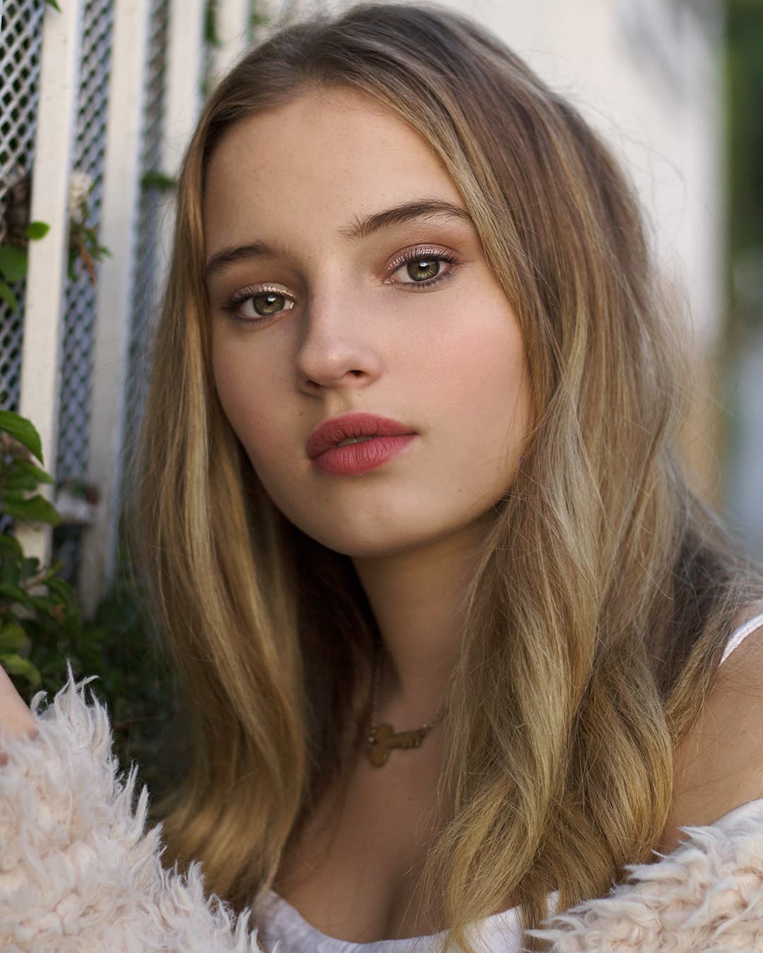 Girl against white fence and flowers.