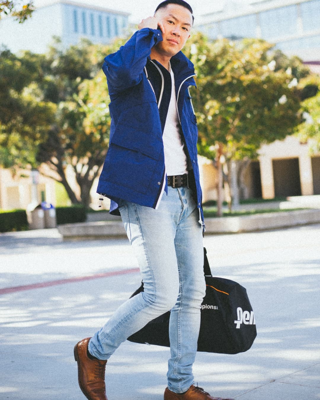 Man posing in windbreaker while walking on phone with a bag.