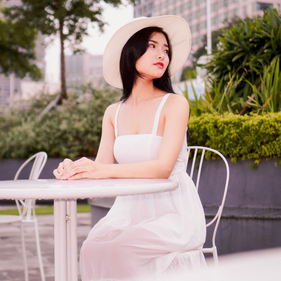 Woman sitting at table with white dress and hat looking backwards.