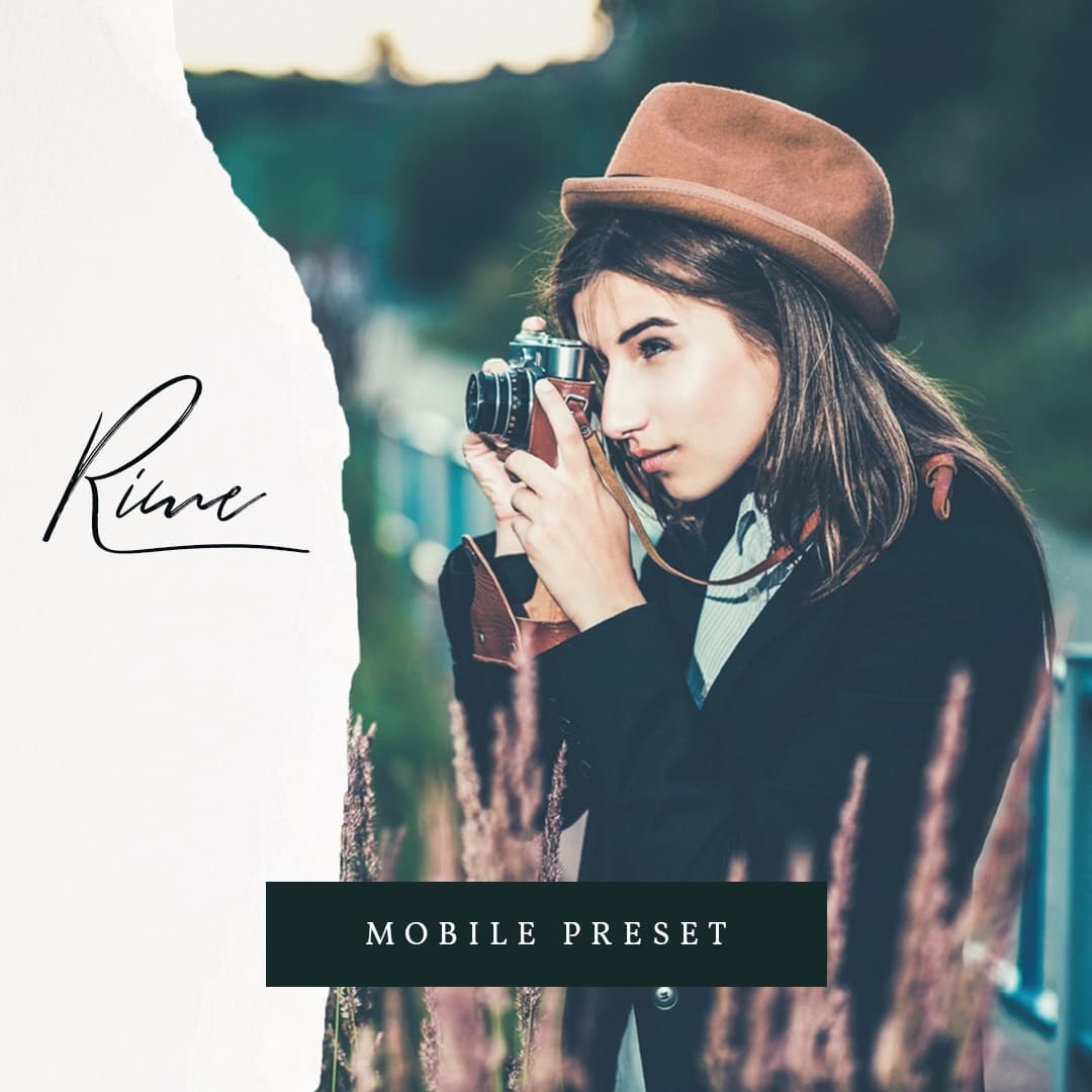 Woman wearing suit and hat holding camera to her eye.