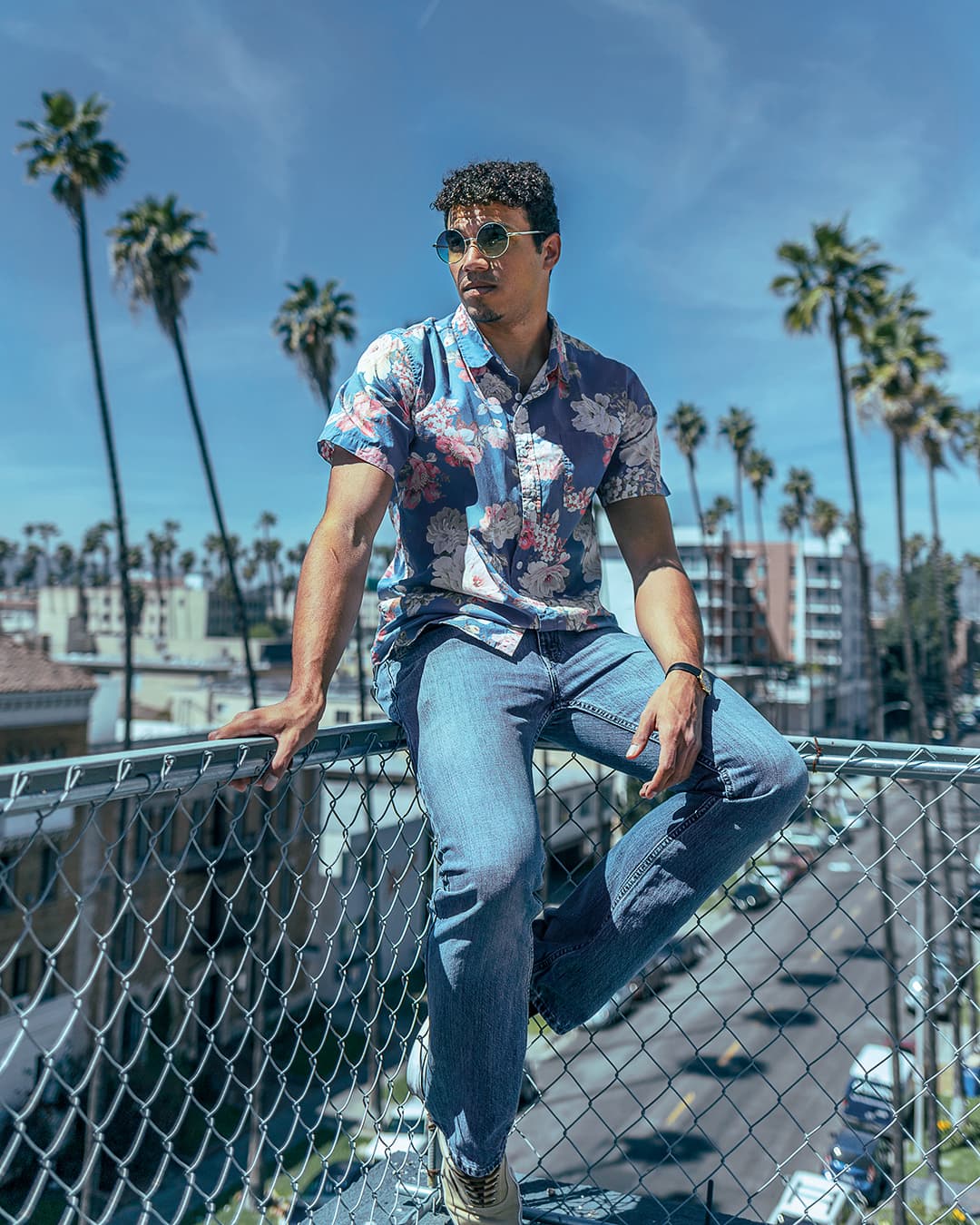 Subject sitting on fence framed between trees Man sitting on fence framed between palm trees.