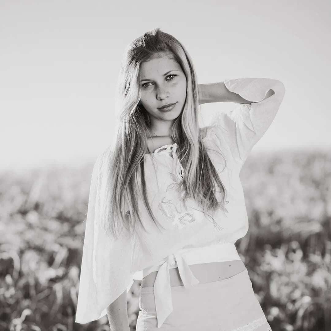 Blonde teenage girl looking at camera with hand on her hair.