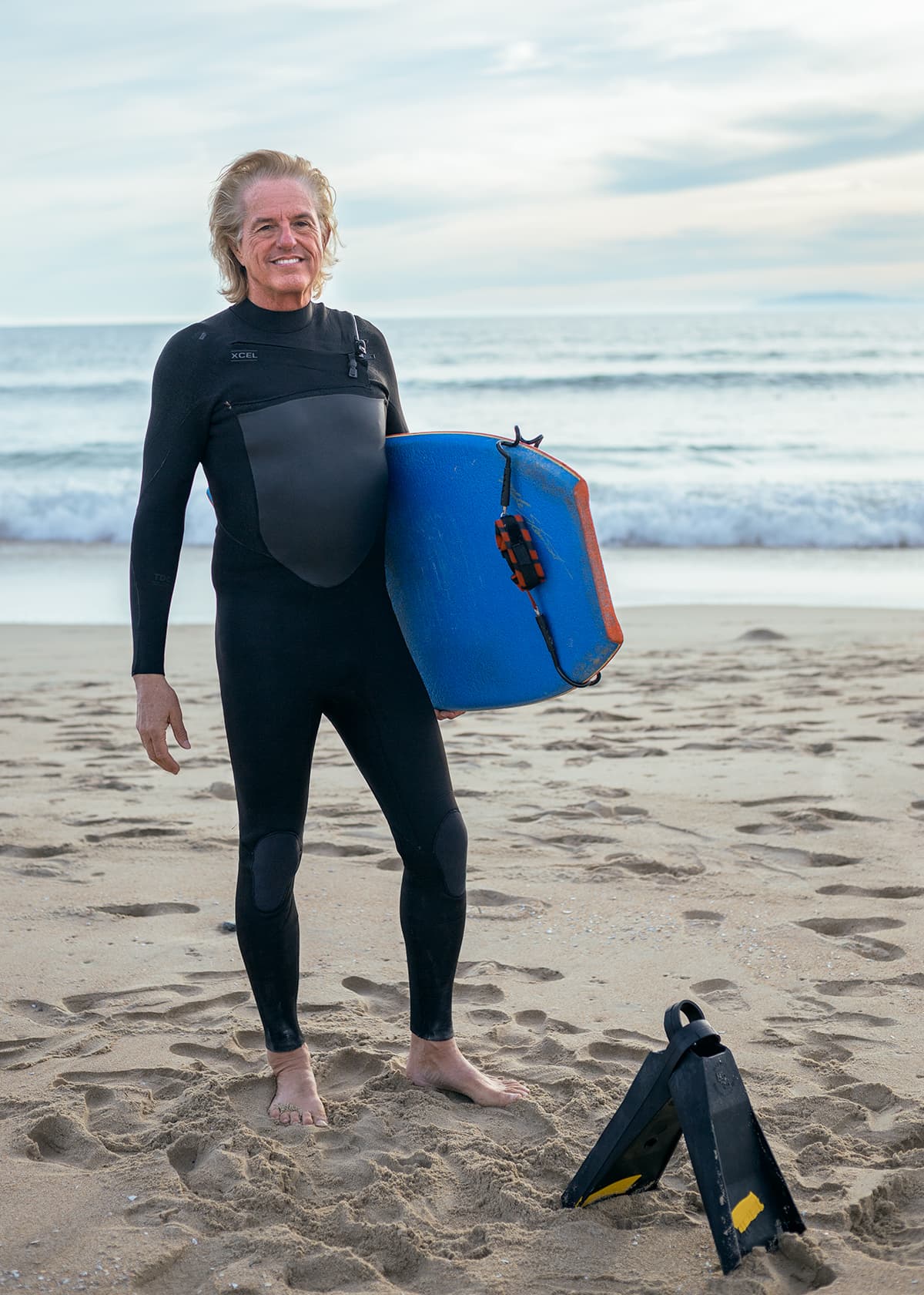 Foreground depth Man standing in wetsuit with boogie board and fins.