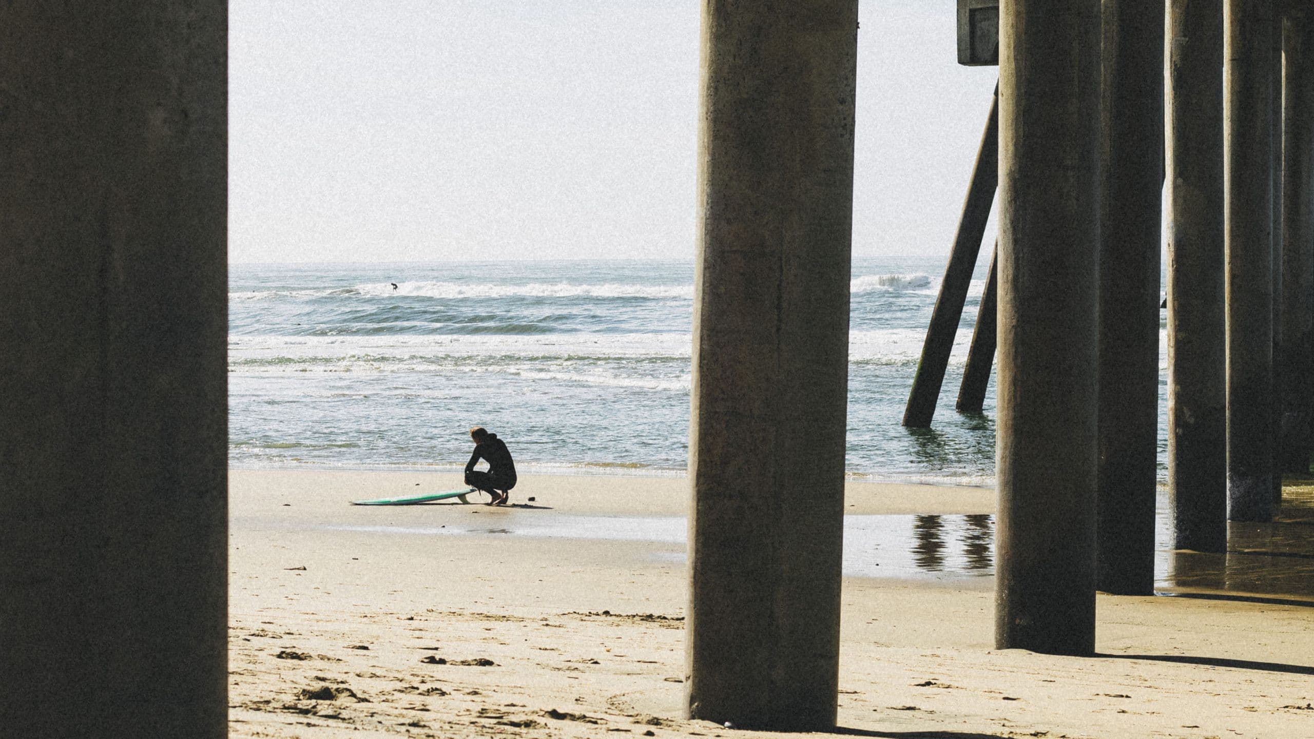 Surfer as the subject Surfer being framed between the pier columns.
