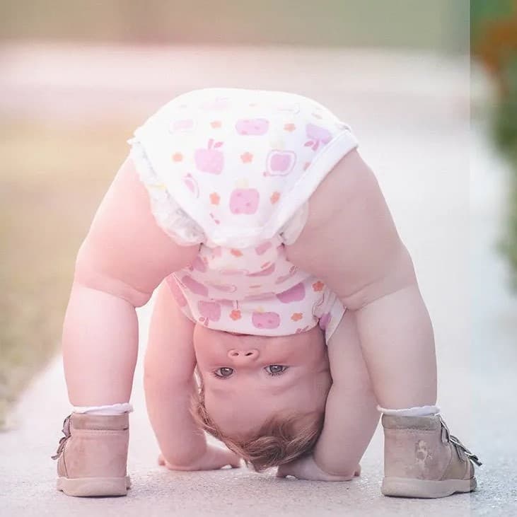 Baby looking through legs with hands on ground.