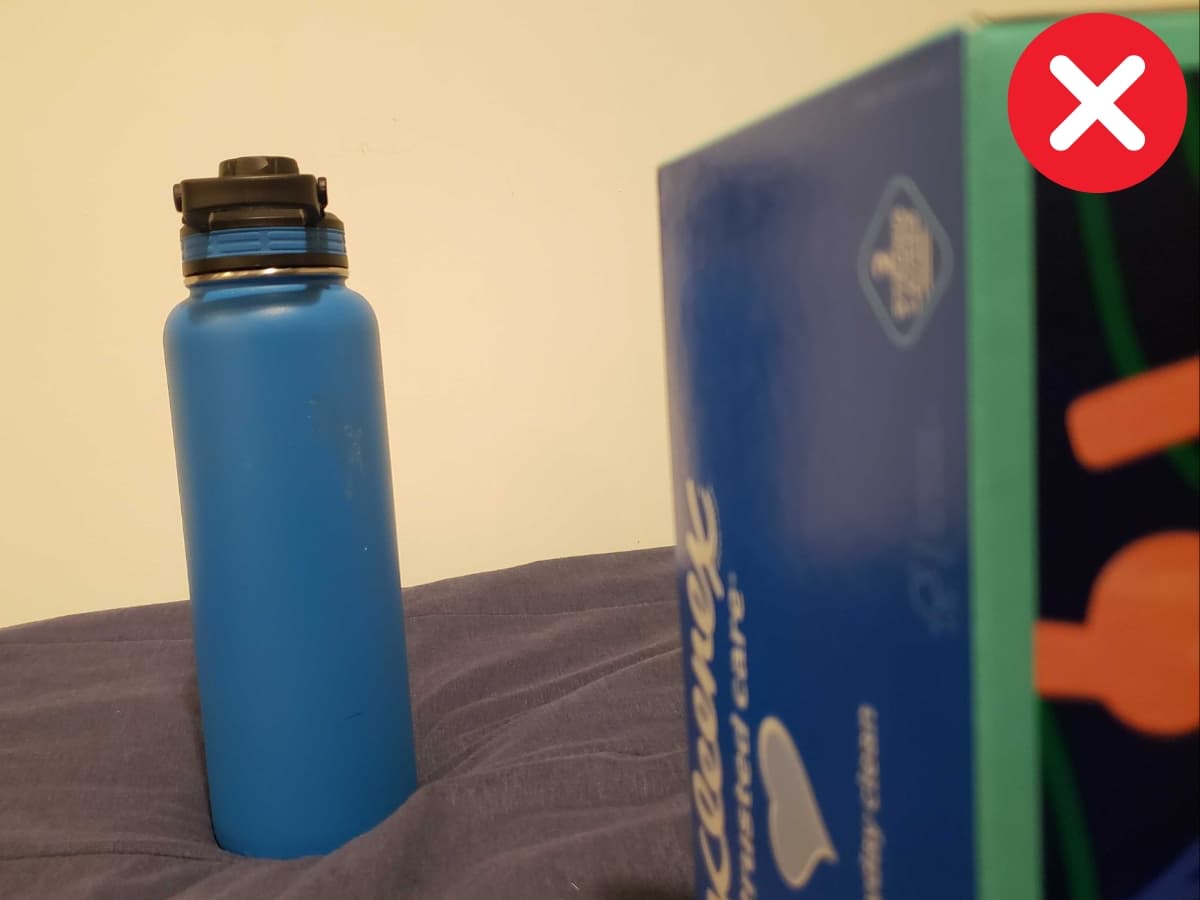 Incorrectly framing on one side Water bottle next to tissue box on a bed.