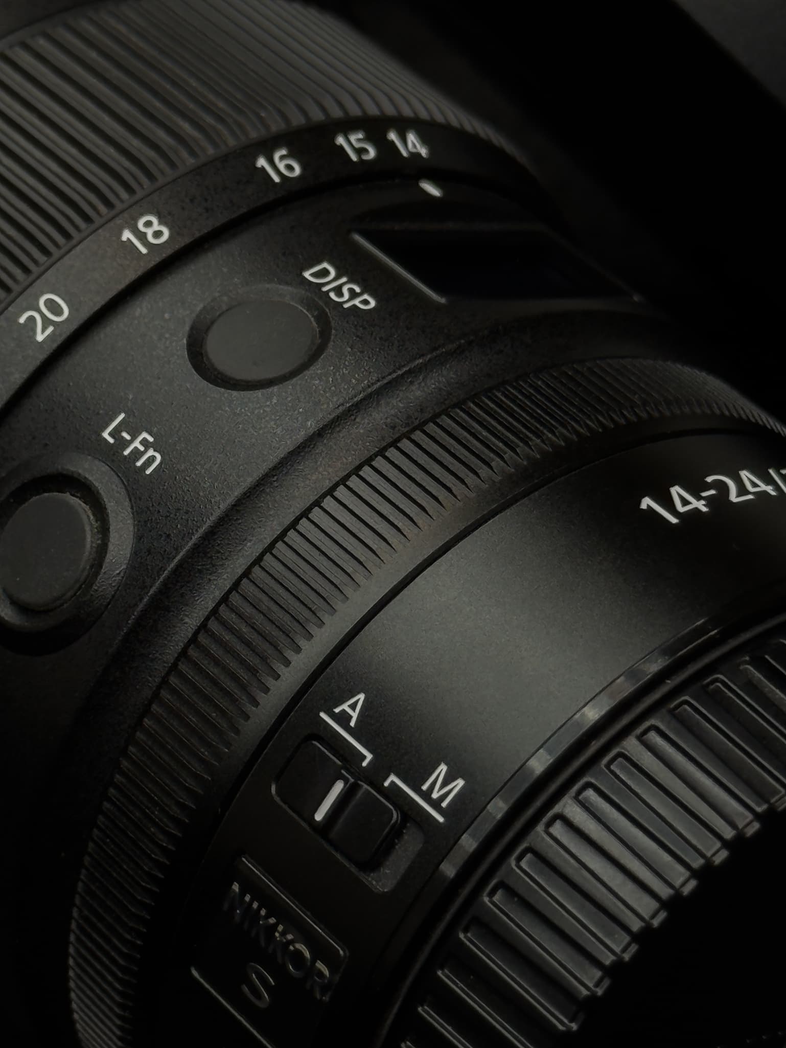 Shot highlighting the physical material of the Nikon Z 14-24mm f/2.8 S split between the cold metal lens mount base and the premium matte engineered polymers used to keep the chassis lightweight