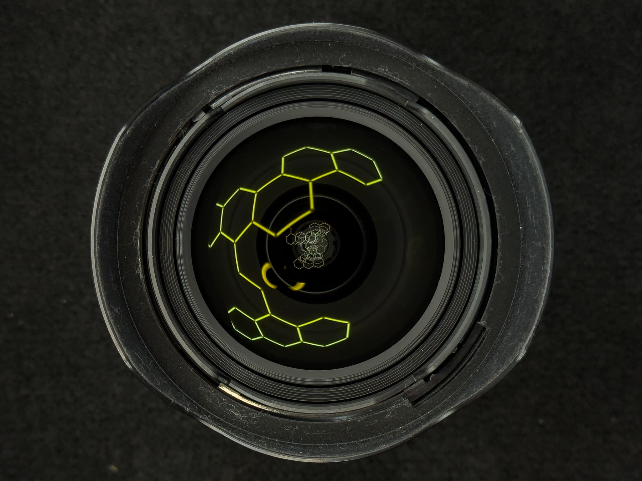 Tight accent shot of the specialized bulbous front glass element catching a straight grid light to highlight the precise double-sided aspherical lens molding on the Nikon Z 14-24mm f/2.8 S